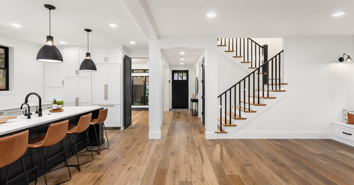 A large open concept living area. There is a kitchen island with chairs on one side and stairs upwards on the other.