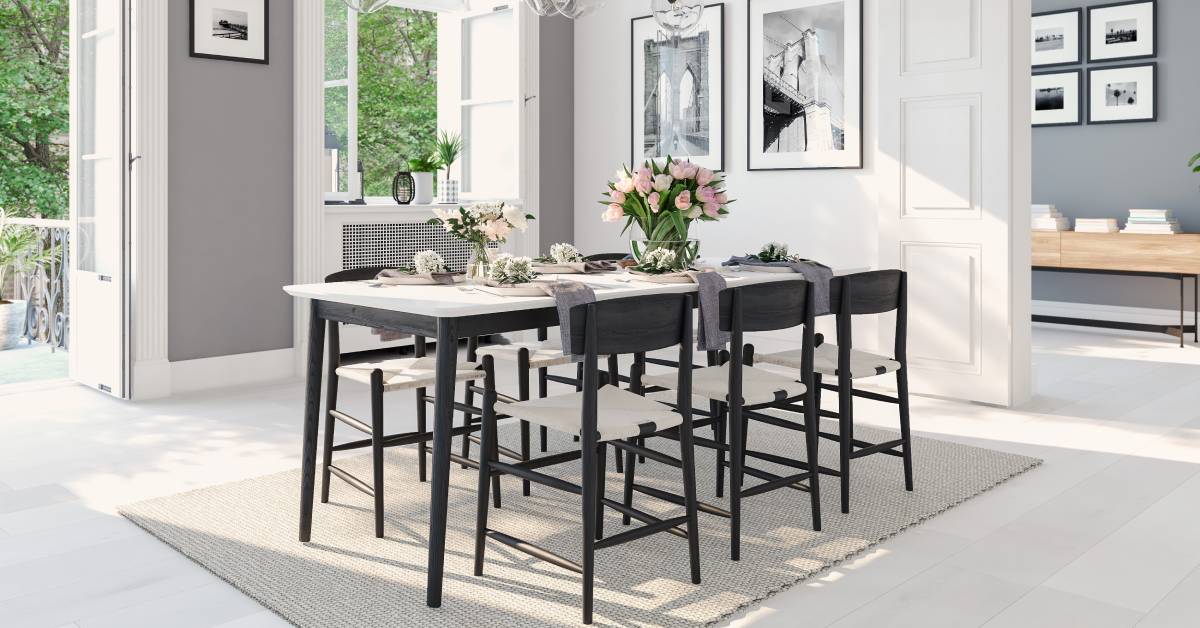 A brightly lit dining room with a black table and chairs in the middle. A set of white doors with glass lead outside.