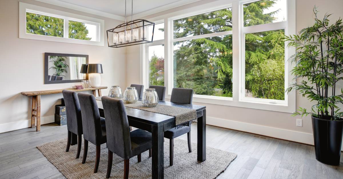 A luxurious, modern dining room. A table with six chairs sits in the middle of the room in front of a large window.